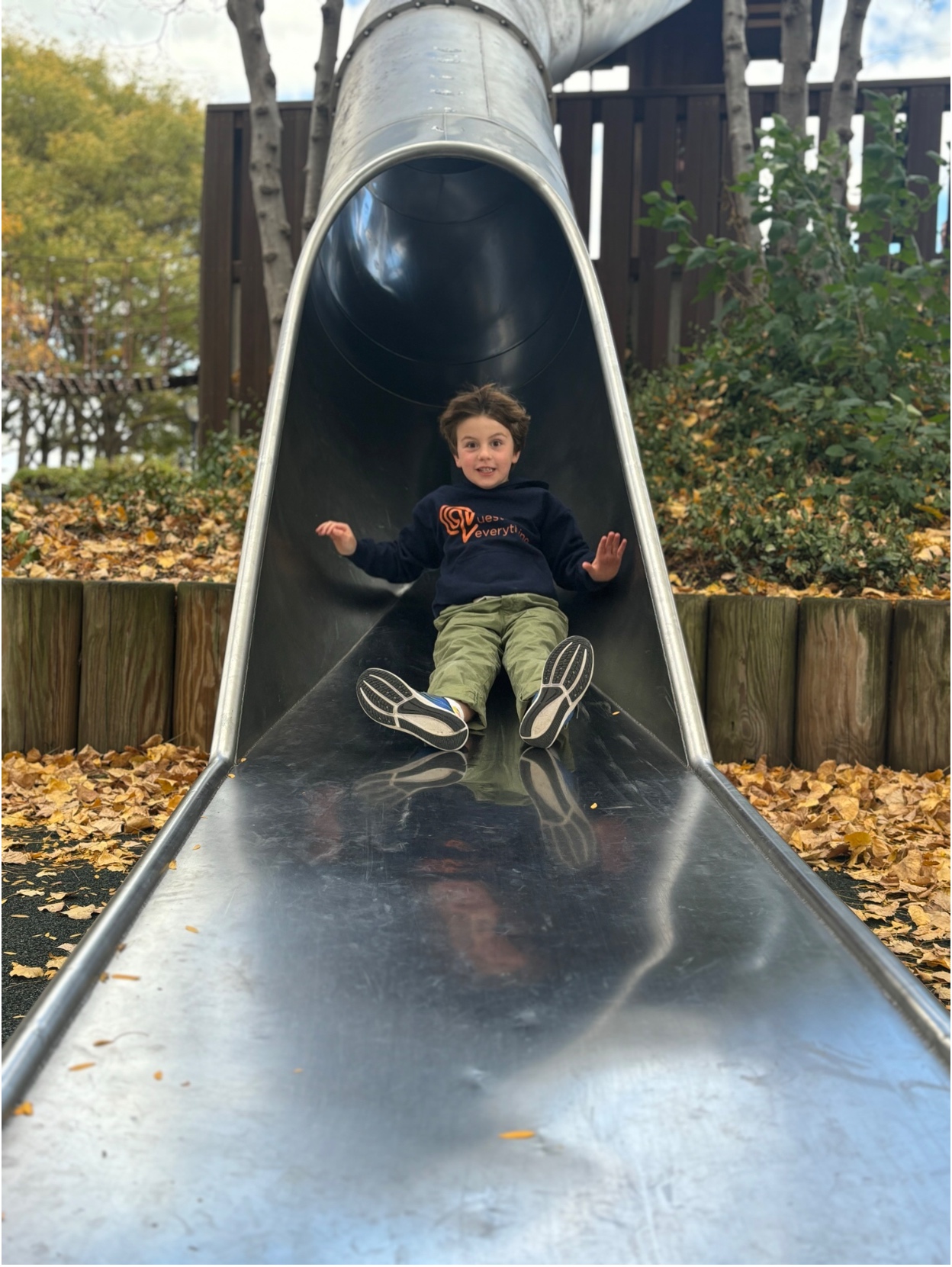 A young Hudson School student sliding down a metal playground slide amid autumn leaves