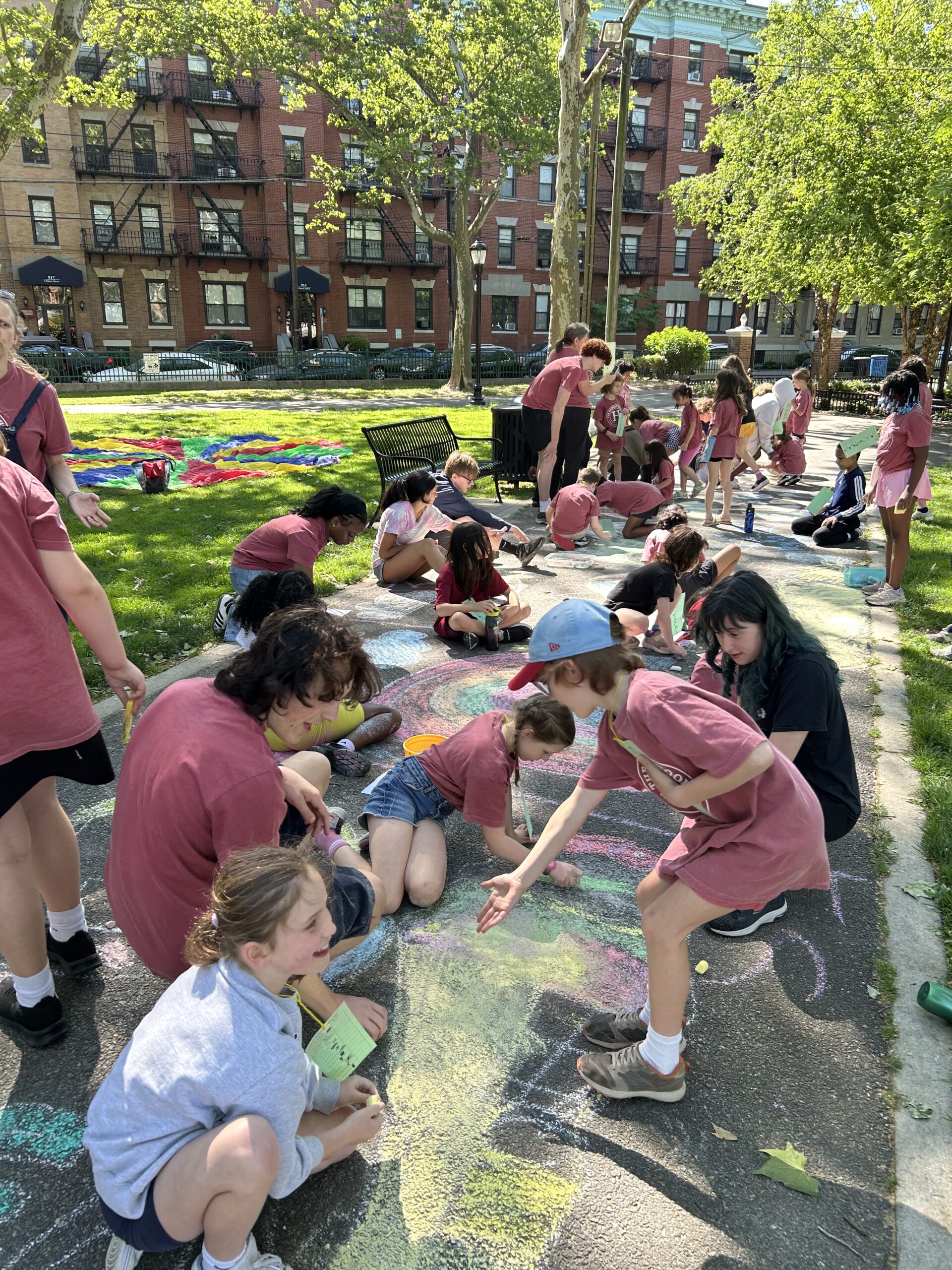 Hudson School students in maroon T-shirts making colorful sidewalk chalk art in a Hoboken park