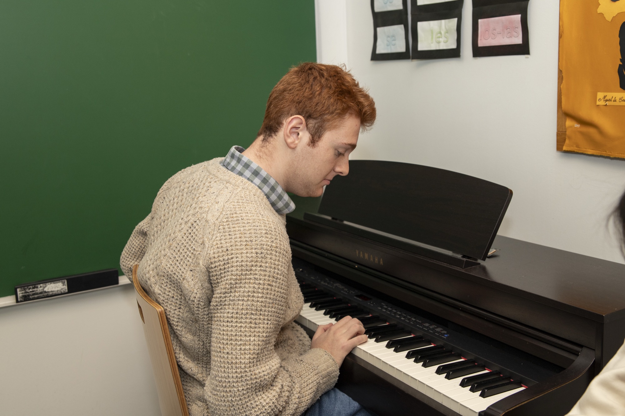 Teacher playing piano with Upper School students gathered nearby