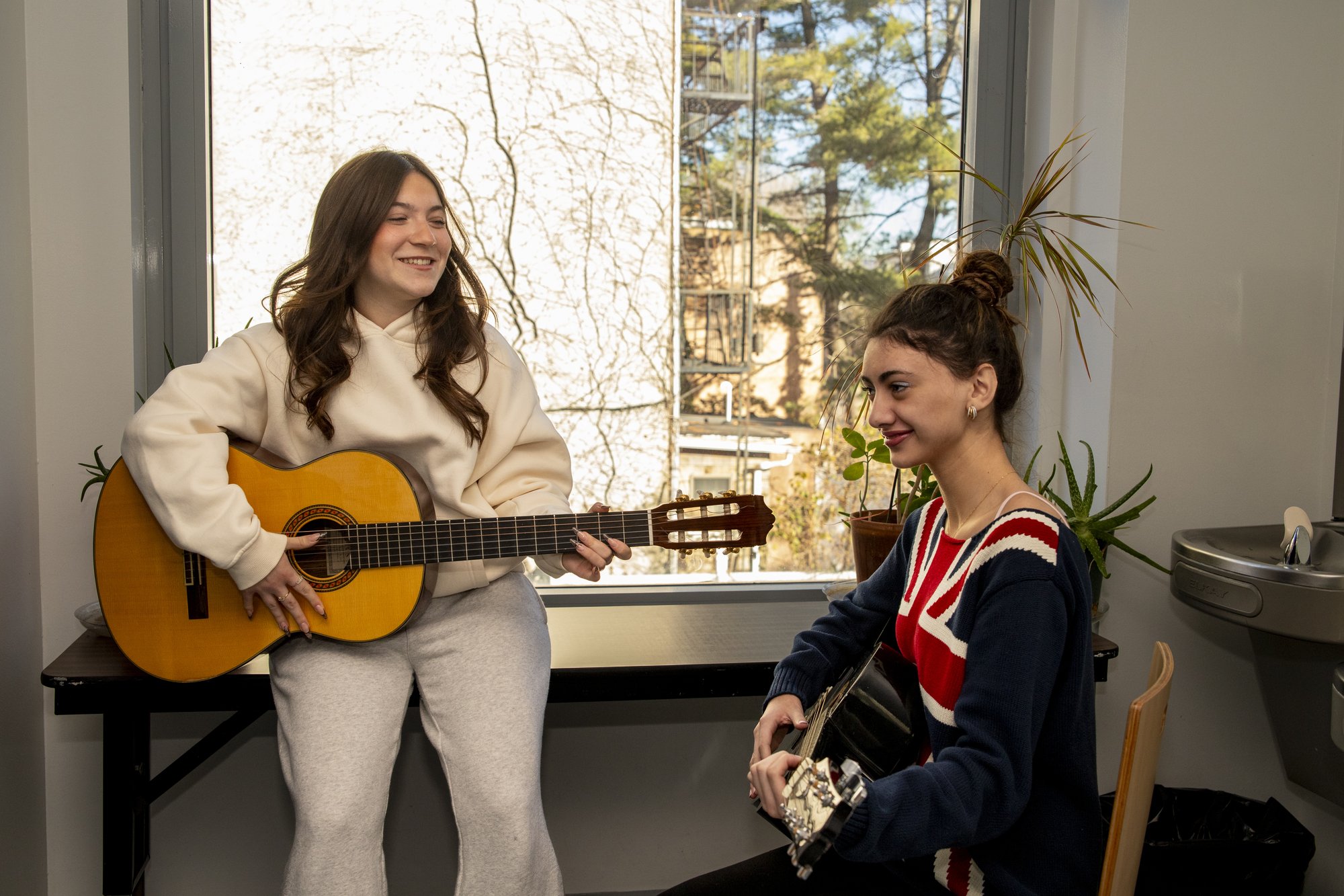 Two Hudson School students playing acoustic guitars together by a bright window