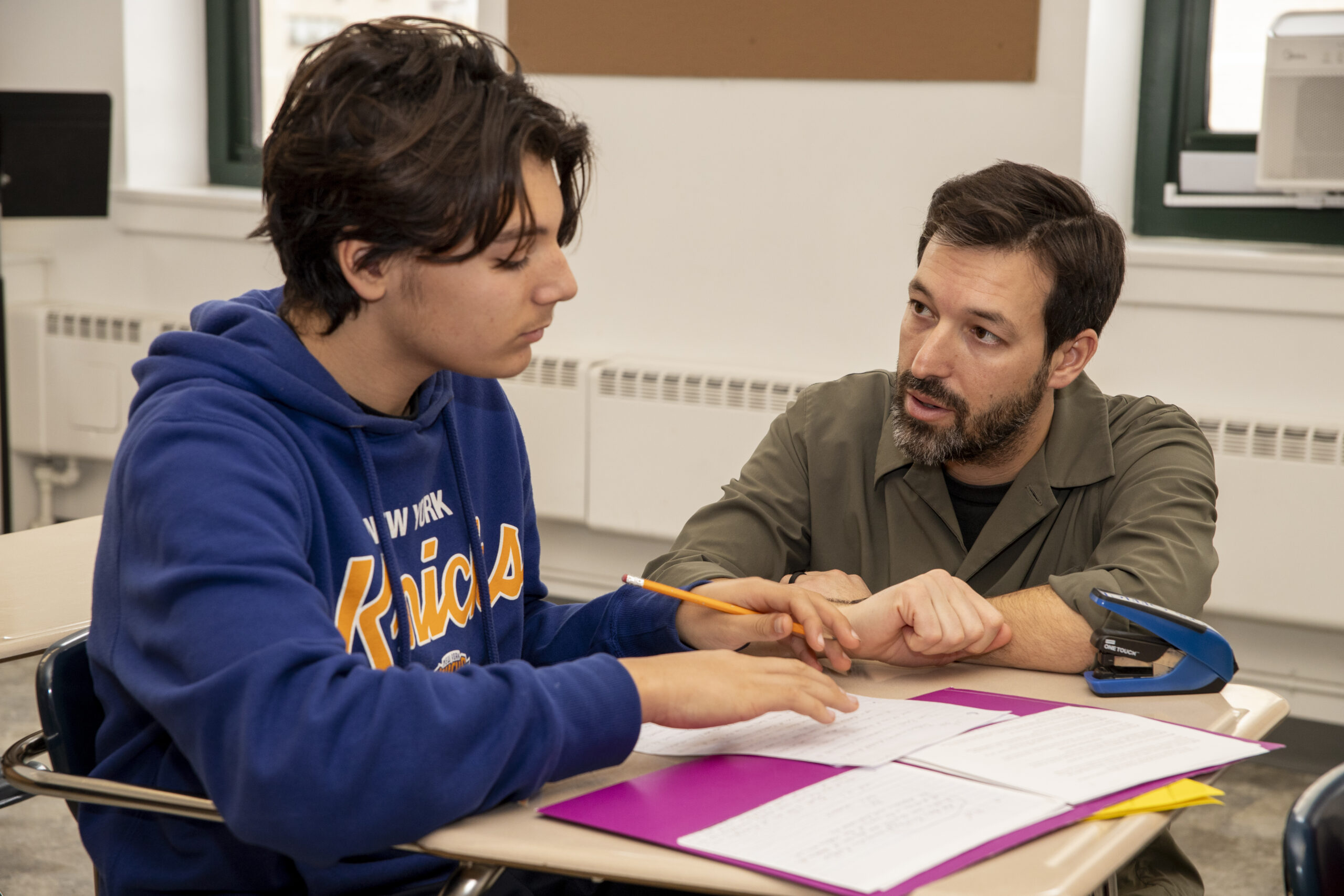 A Hudson School teacher working one-on-one with a student at a desk, reviewing written work together.