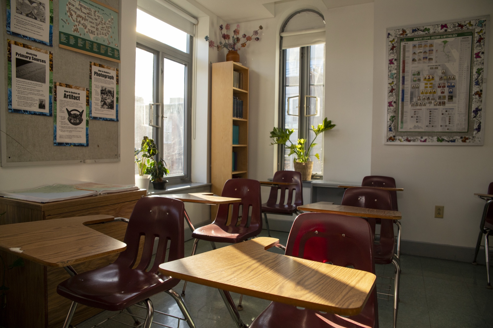 Sunlit empty classroom with wooden desks and plants at The Hudson School
