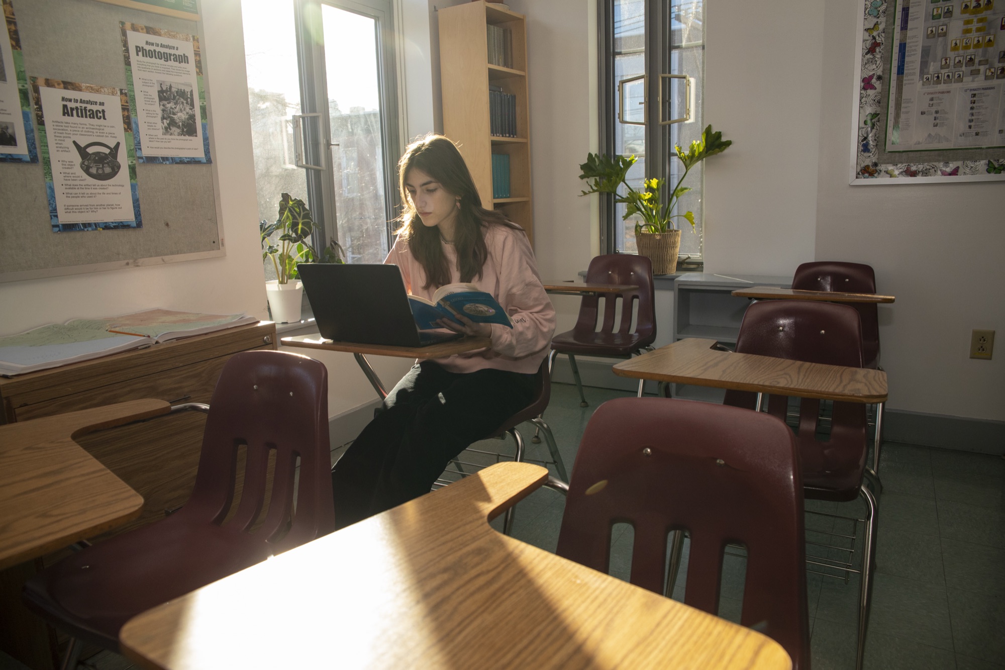 A female Hudson School student writing at a desk in a warm classroom