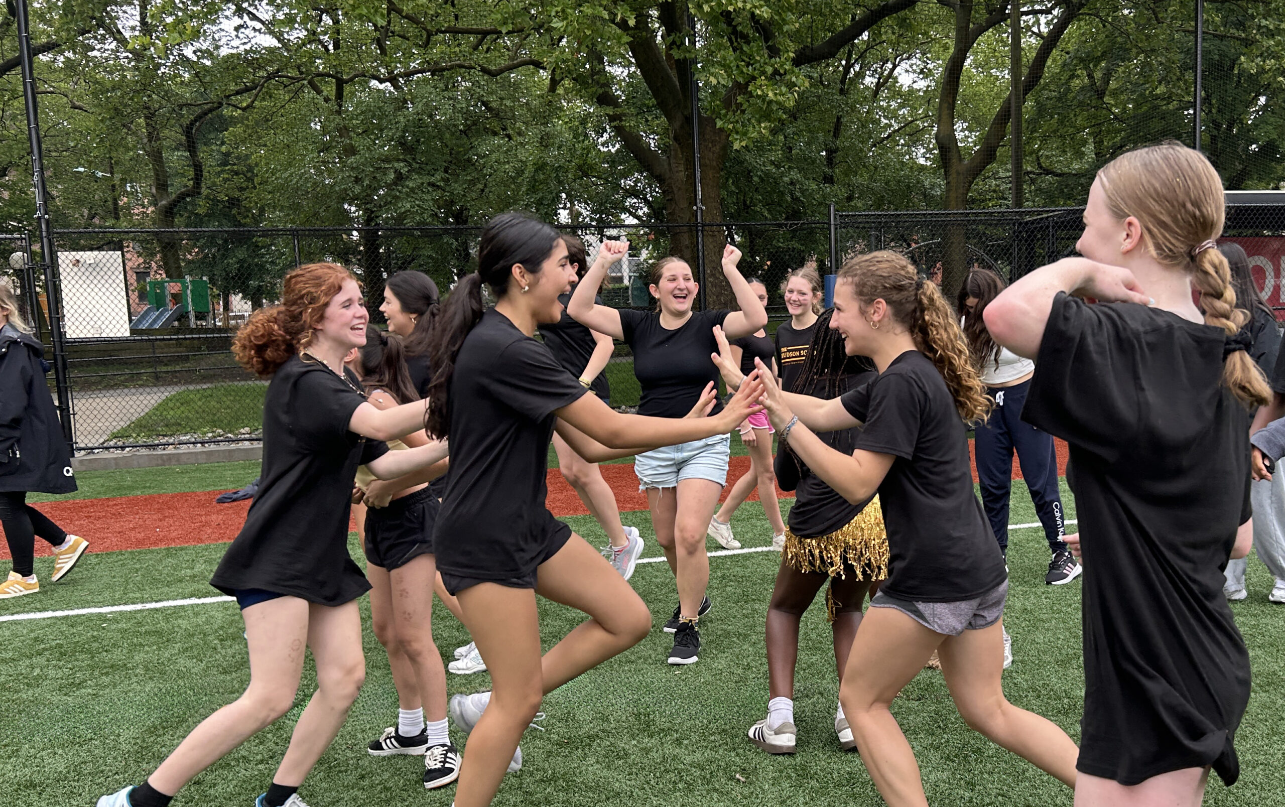 A group of Hudson School girls celebrating with high-fives and cheers on an outdoor turf field